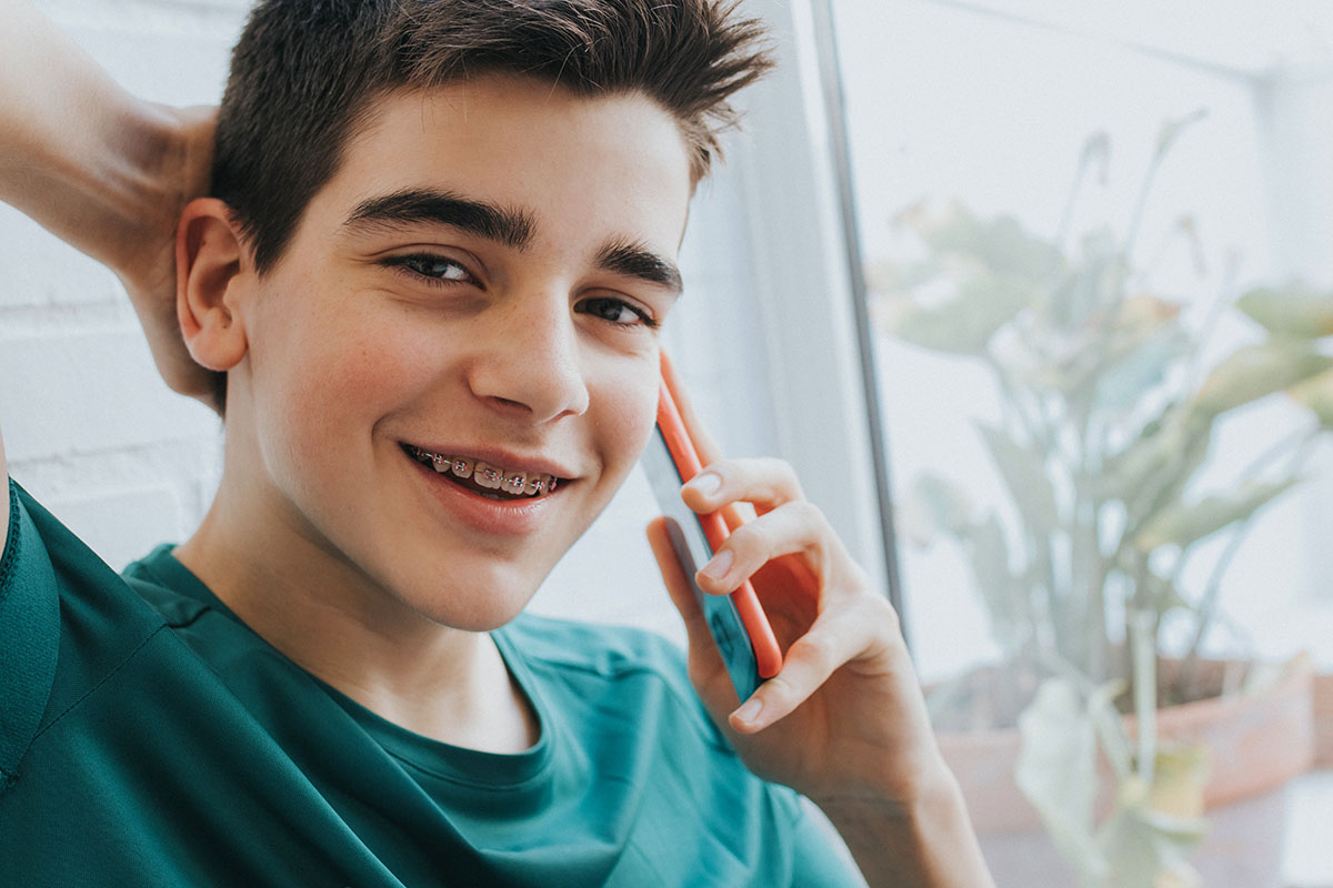 Teenage Junge am Telefon lächelt mit klassische Zahnspangen